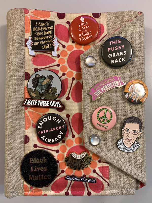 a fabric folio with sassy political pins on it