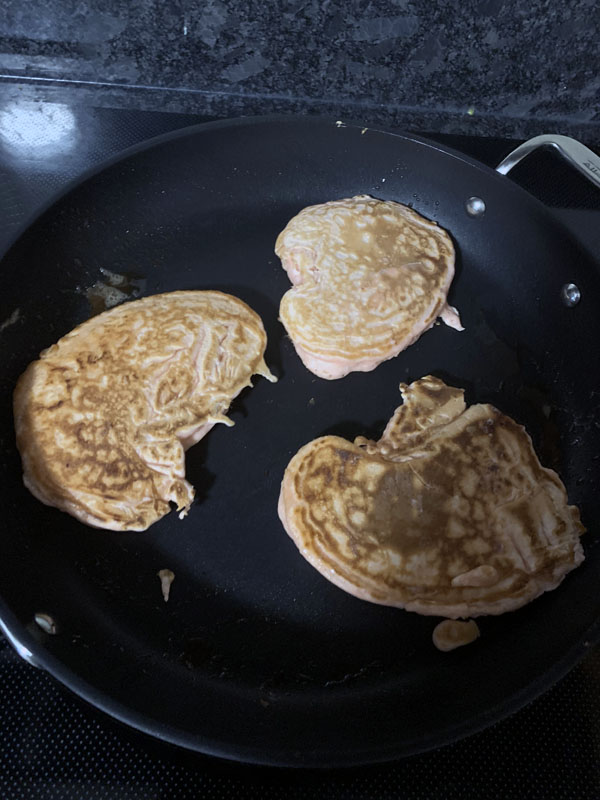 pancakes in a pan. they are supposed to be heart shaped but are not.