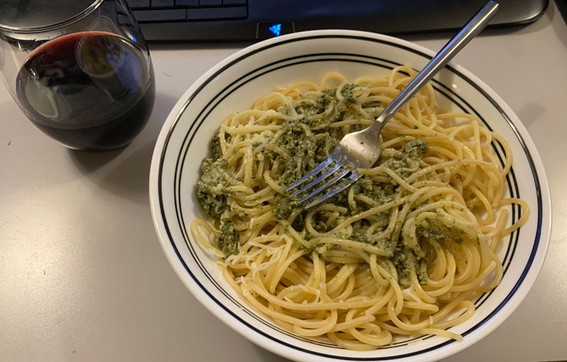 a too-large bowl of spaghetti and pesto, with a glass of red wine on the side