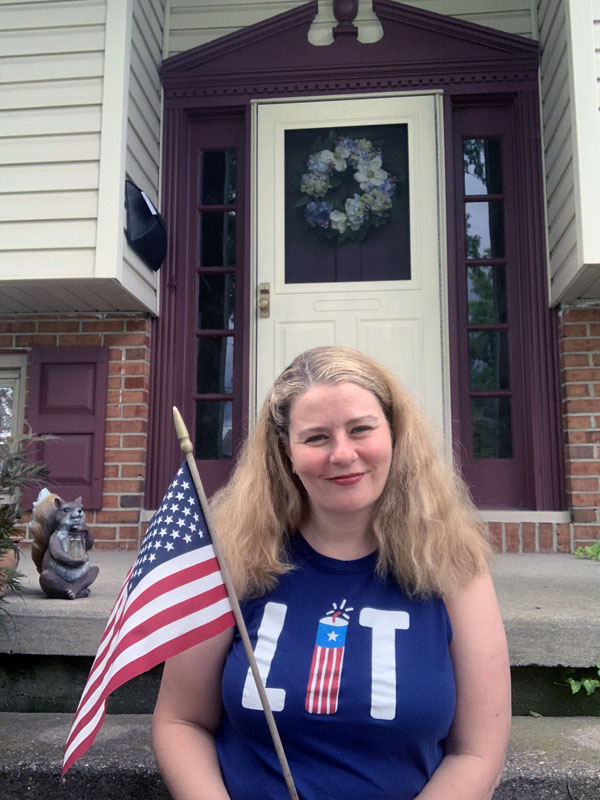 Kim, sitting on her front step, holding a flag and wearing a tee that said "lit" where the I is a firecracker, because Kim is extra like that.