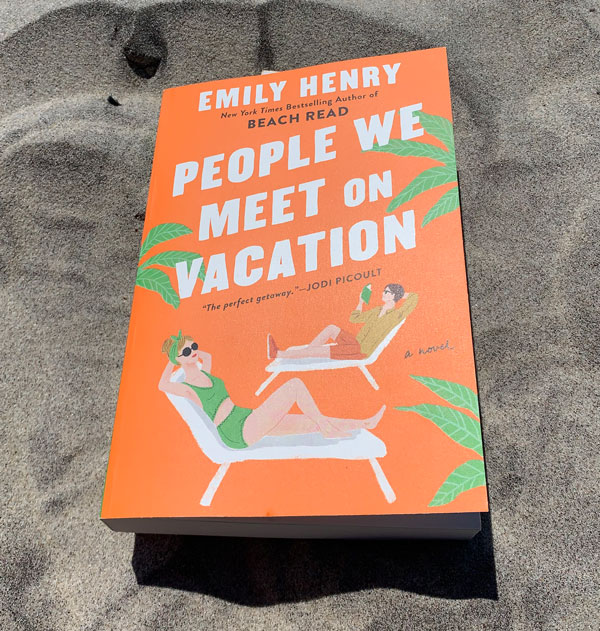 The book People We Meet on Vacation on top of sand.