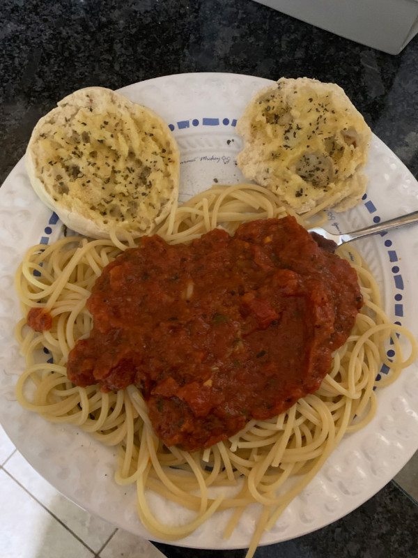 A serving (okay many servings) of spaghetti with two garlic bread rounds positioned above it, making a mickey mouse shape.