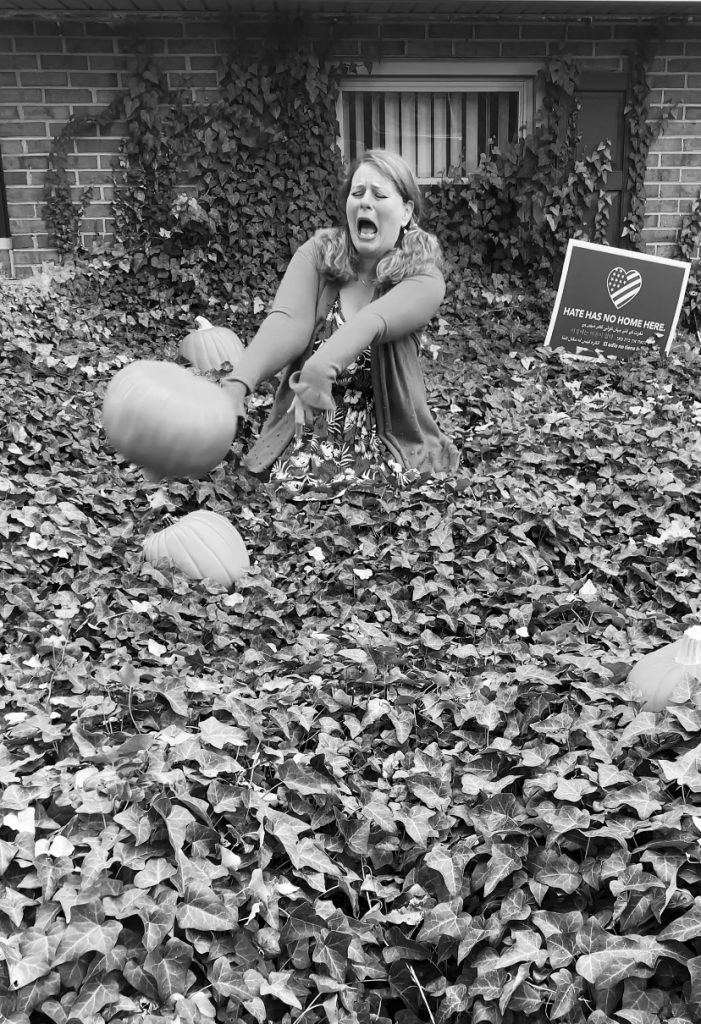 still shot of Kim sitting in her ivy patch tossing a fake pumpkin in autumnal equinox despair