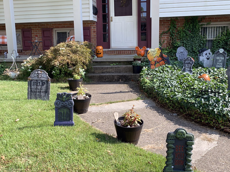 foam gravestones on the other side of a front walkway. there are orange pumpkin decorations on the front porch