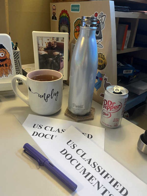 kim's work area, with three different types of beverage and a few pieces of paper with "US classified documents" on them.