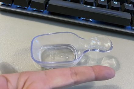 a clear plastic scoop with my index finger next to it for scale. It's smaller than my finger