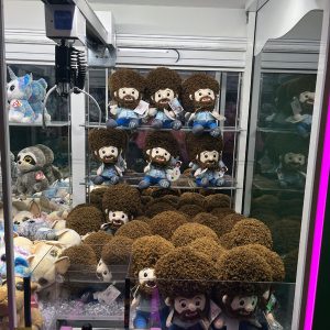 a crane game full of adorable bob ross plushies