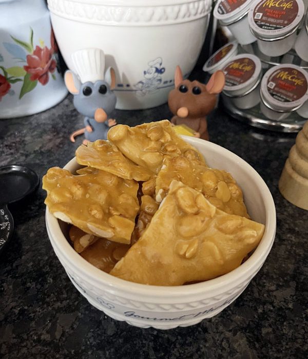 a bowl of peanut brittle, with Remy and Emil figurines watching approvingly