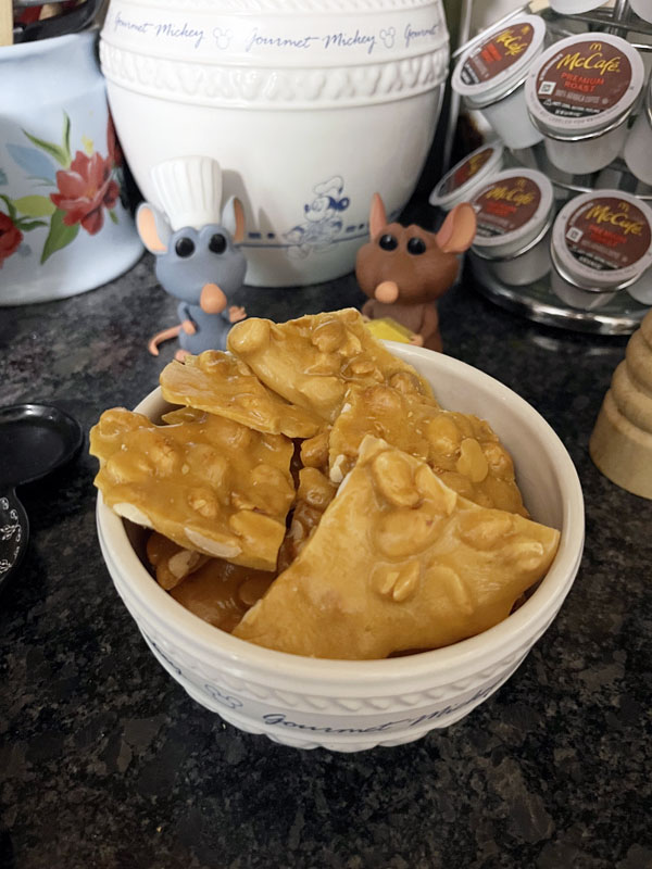 a bowl of peanut brittle, with Remy and Emil figurines watching approvingly