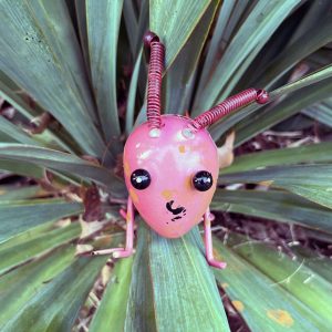 a pink metal sculpture of a bug in a plant, found while walking through my neighborheed