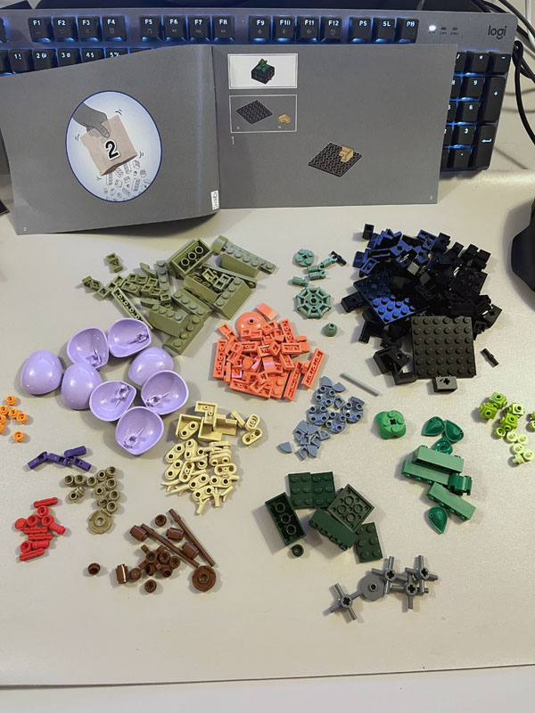 Lego pieces in lilac, various shades of green, coral, black, and brown.