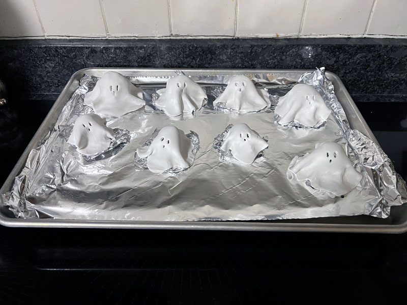 a small group of clay ghosts on a cookie sheet