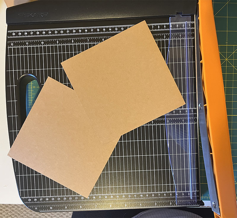 two six inch by six inch squares of light brown paper on a paper cutter