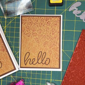 a brown card with a stamped floral back ground and a die cut 'hello' on the front