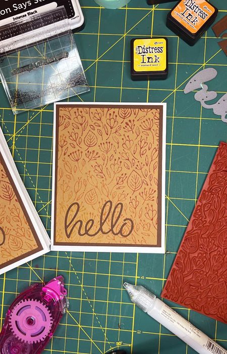 a brown card with a stamped floral back ground and a die cut 'hello' on the front