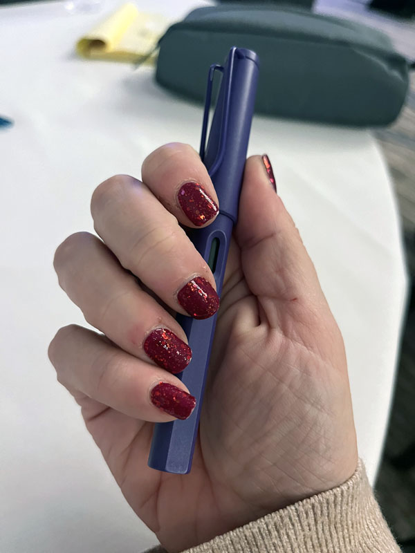 kim holding her pen, but showing off her cranberry glitter color street nail strips