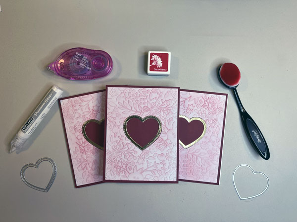 three homemade valentine's day cards. They are embossed, lightly inked with pink ink over the embossing, and have a red heart in the middle