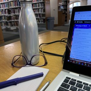 a non-Stanley water bottle, glasses, notepad, pen, and a corner of my laptop at the library