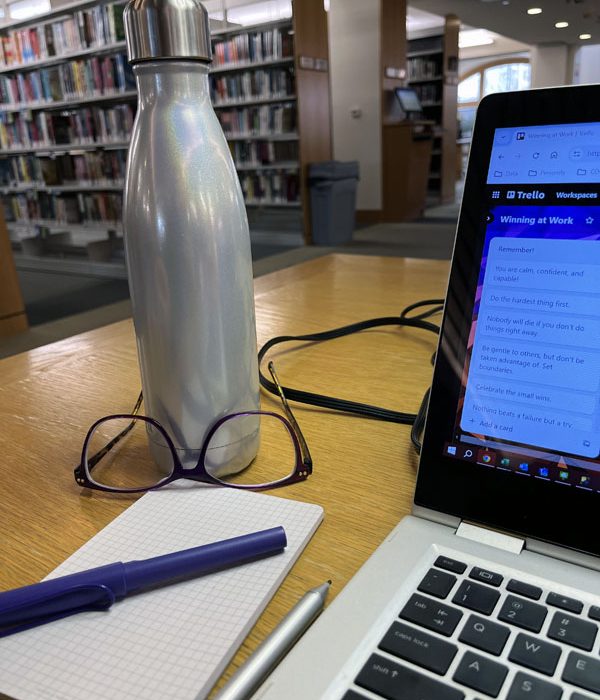 a non-Stanley water bottle, glasses, notepad, pen, and a corner of my laptop at the library