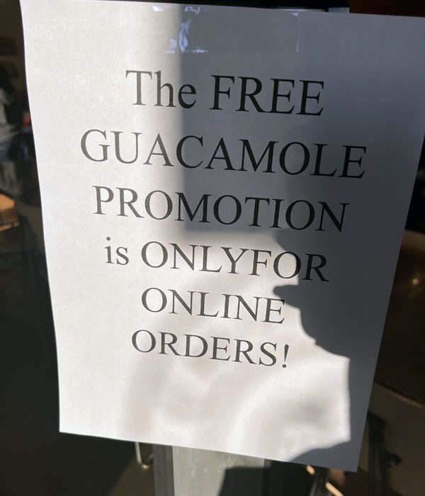 a hastily made flyer taped to the door of Chipotle that says "THE FREE GUACAMOLE PROMOTION is ONLYFOR ONLINE ORDERS!'