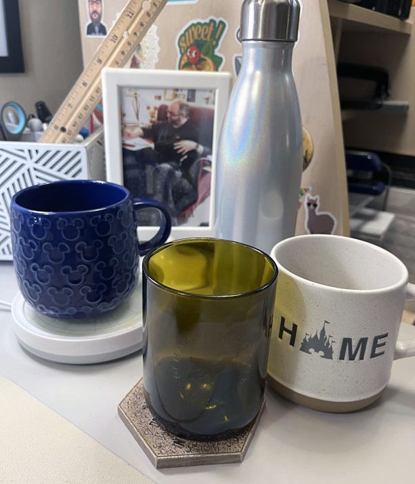 A blue mickey mouse mug, a brown glass, a natural colored mug with "HOME" on it (the o in home is a silhouette of Cinderella castle) and a S'well water bottle.