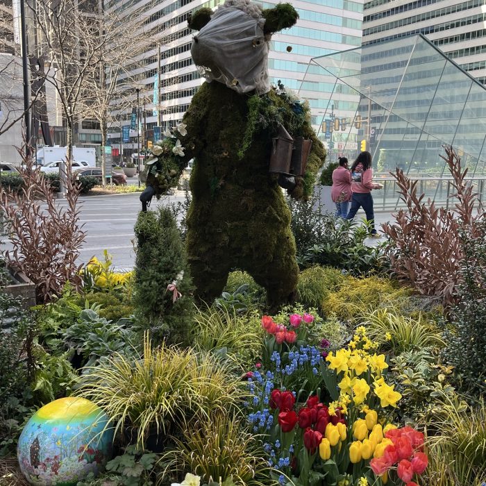 a topiary of a beekeeping cow in Philadelphia. There are tulips in front of it.