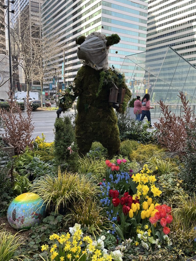 a topiary of a beekeeping cow in Philadelphia. There are tulips in front of it.