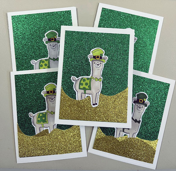 a display of handmade cards with a green/gold glitter background and a festive llama cutout on them