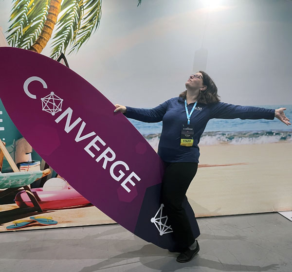 kim straddling a foamcore surfboard in front of the conference selfie wall after the conference was finished
