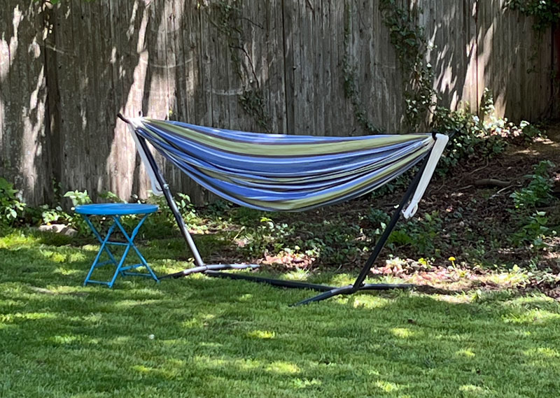 a blue and green striped hammock on a  hammock stand with a bright blue table next to it. It's hammock season again!