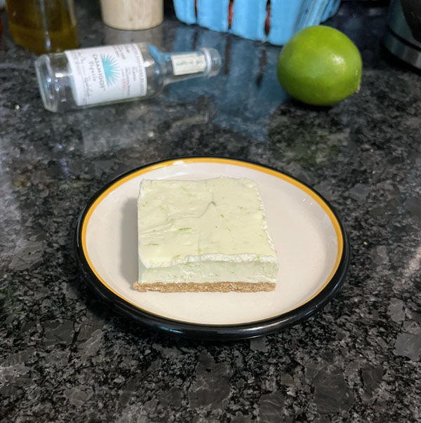 one serving of margarita cheesecake bites, with an empty mini tequila bottle and a lime in the background