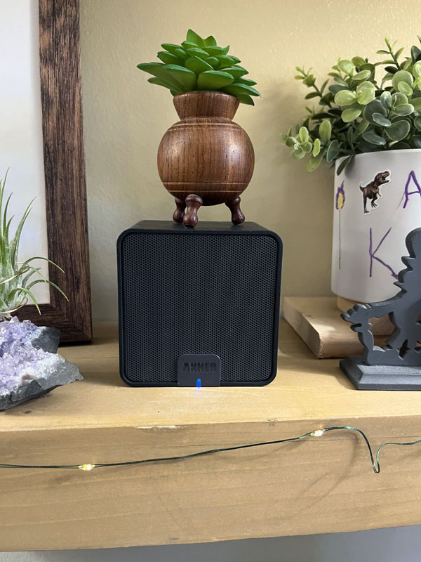 a bluetooth speaker on a shelf with a tiny fake succulent on top and some fairy lights winding by