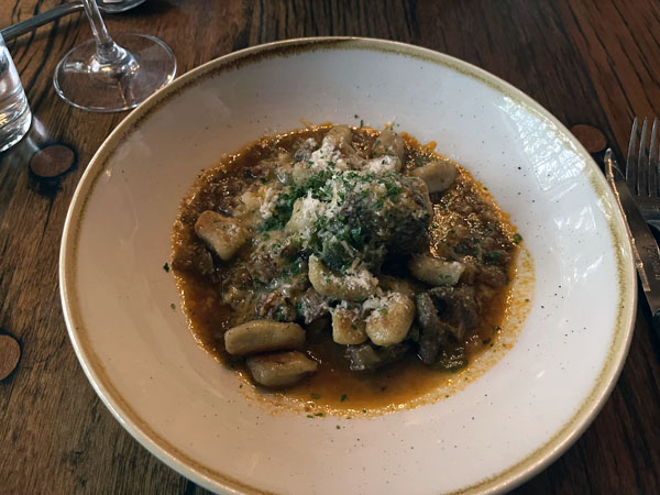 a bowl of meat and gnocchi, topped with shaved cheese and fennel