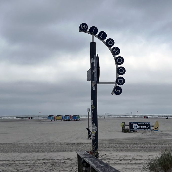 a sign that says "Wildwood" leading to a very cloudy beach