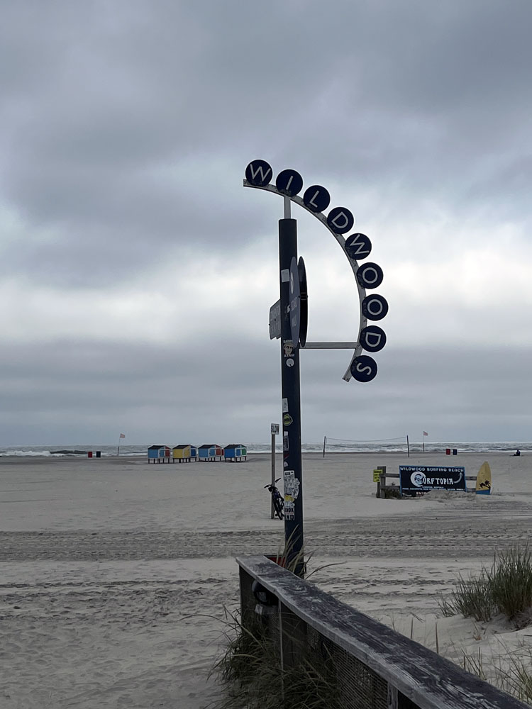 a sign that says "Wildwood" leading to a very cloudy beach