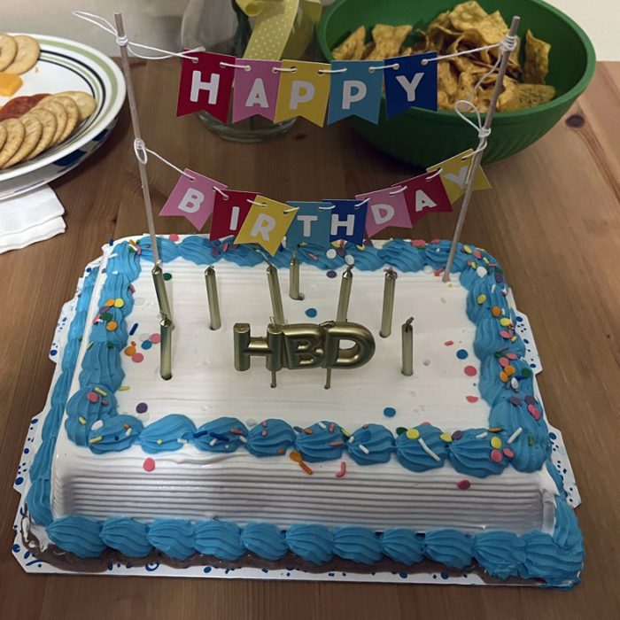 an ice cream cake trimmed in blue, with Happy Birthday pennants and a bevy of candles.