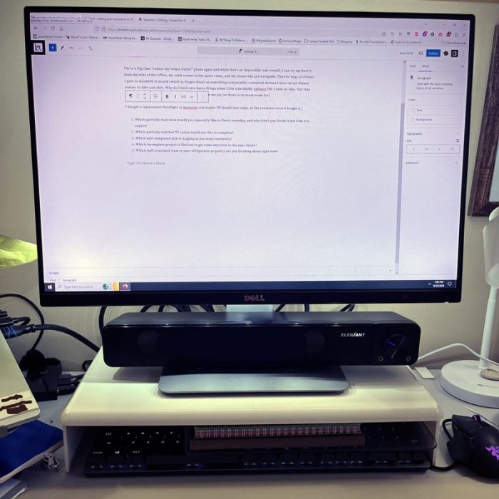 a monitor upon a plastic stand with a shelf. The keyboard is pushed beneath it