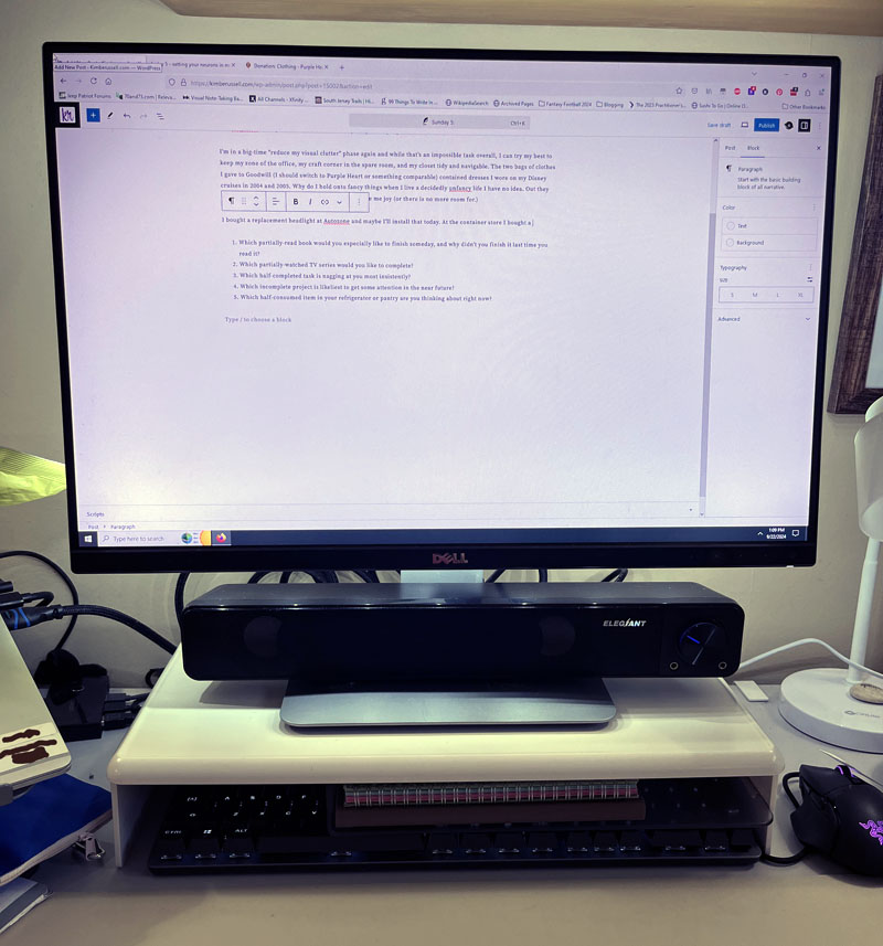 a monitor upon a plastic stand with a shelf. The keyboard is pushed beneath it