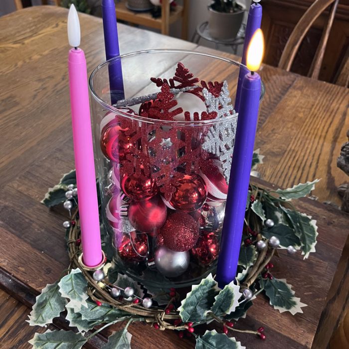 an advent wreath with four battery-operated candles. One purple candle is lit, the other three (two purple, one pink) are not.