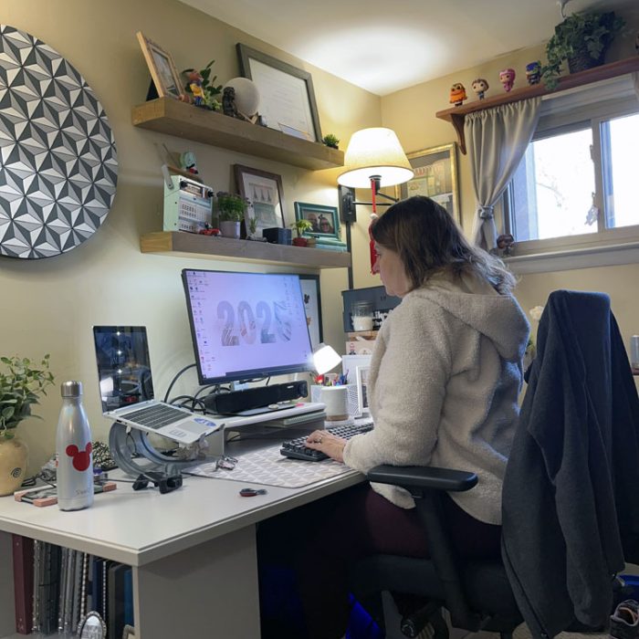 kim at her desk. A painted spaceship earth is on the wall. It's a pretty desk. She's wearing a white fleece pullover hoodie which makes her look hunchier than she is. This is a completely staged photo.