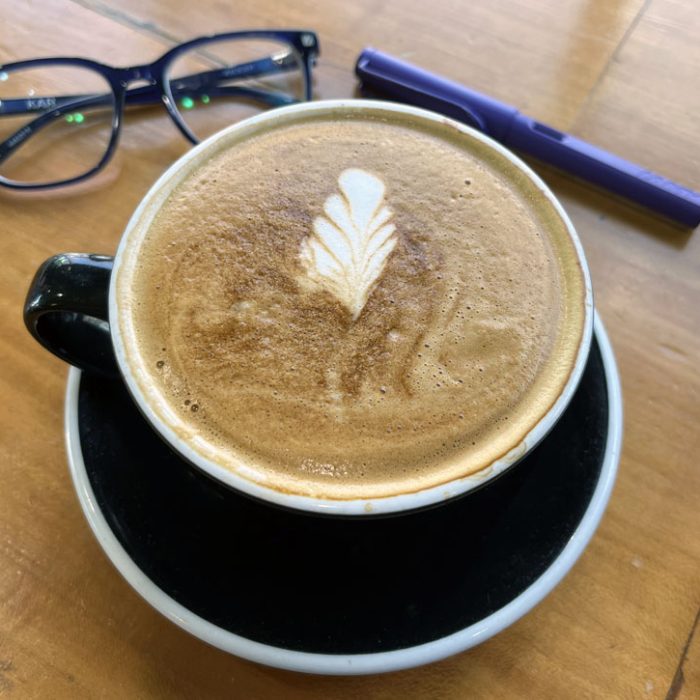 a vanilla-almond late with leaf latte art on top. My glasses and fountain pain are purposefully placed on the wooden table behind the cup because this is how we on the internet manipulate you into thinking everything is perfect