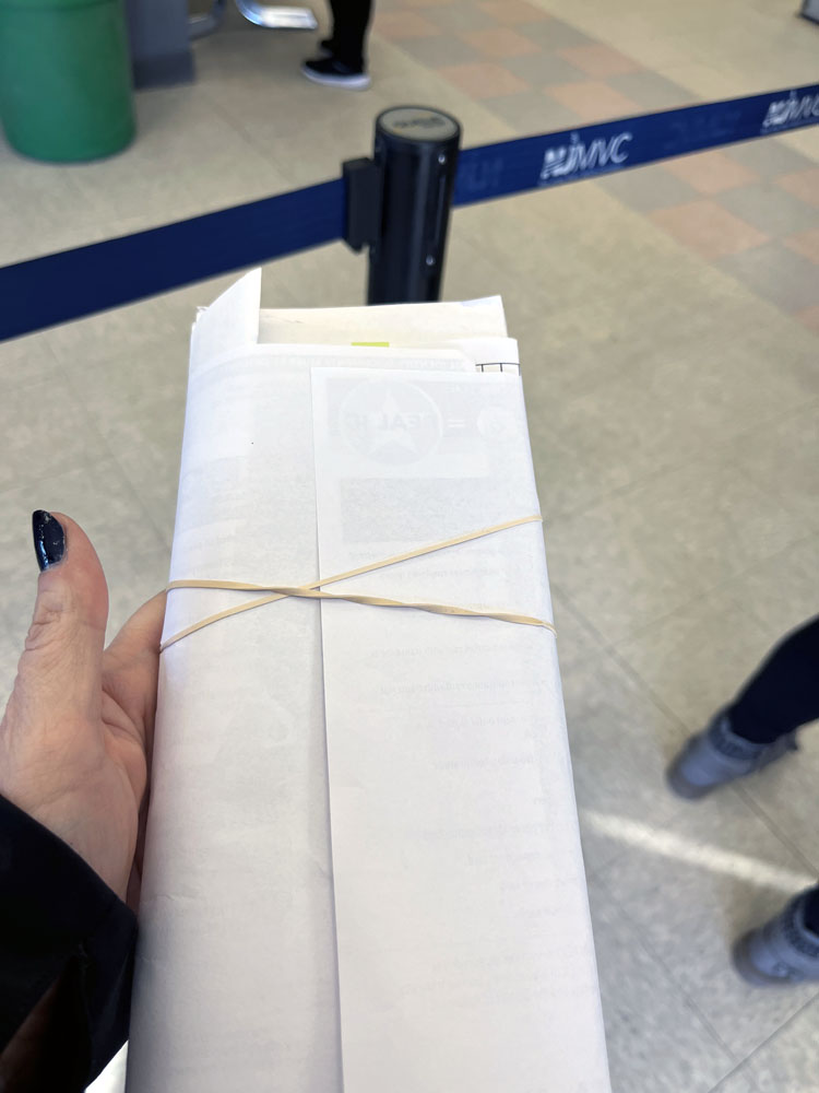 kim holding a packet of documents rubberbanded together. you can see the NJMVC stanchion behind it. My nails are a painted blue!