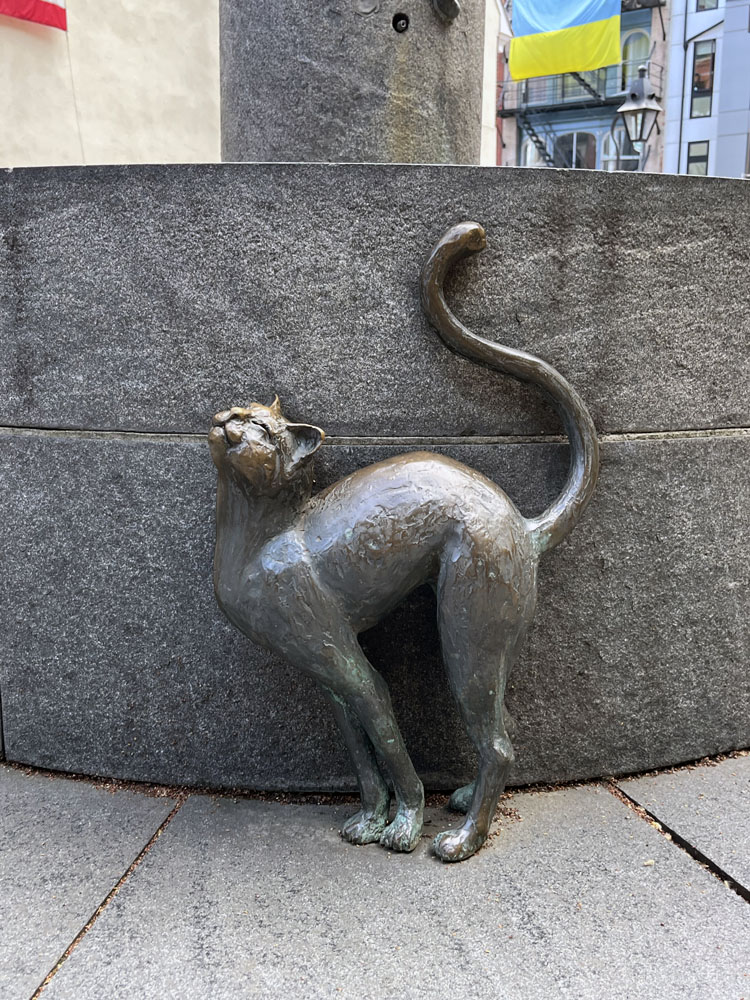 A small statue of a cat rubbing up against a fountain