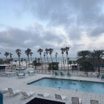 Foreground: hotel balcony bars. Middle ground: a rectangular pool with a dozen seagulls frolicking. Background: palm trees, a beach, and the Gulf of Mexico. 