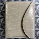 a beige planner cover, closed, with a croco print and a curved flap.