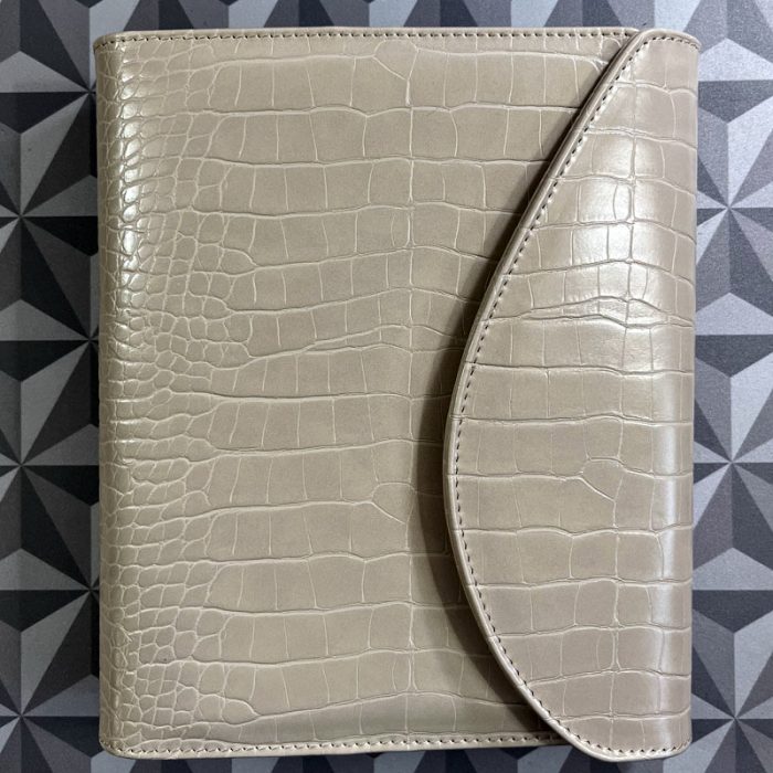 a beige planner cover, closed, with a croco print and a curved flap.