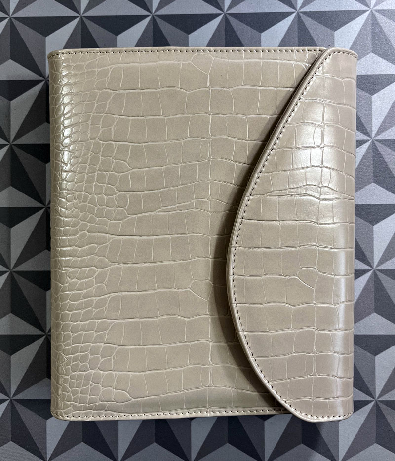 closed beige planner with a faux crocodile texture, resting on a geometric-patterned surface