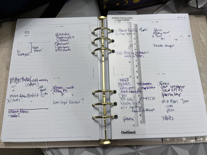 open ring-bound planner showing a filled weekly vertical monday-start spread with handwritten notes and a clear ruler bookmark across the center.