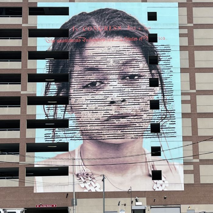 a mural in philadelphia featuring a shoulders-up painting of a young Black woman with the text of the declaration of independence over it. it's called 'declaration'
