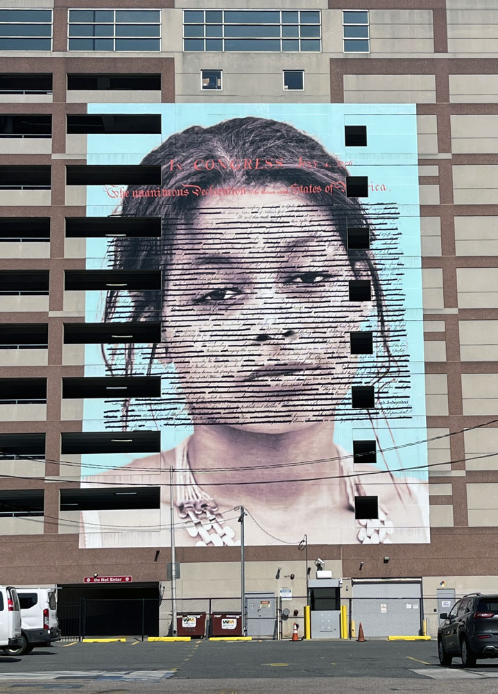 a mural in philadelphia featuring a shoulders-up painting of a young Black woman with the text of the declaration of independence over it. it's called 'declaration'
